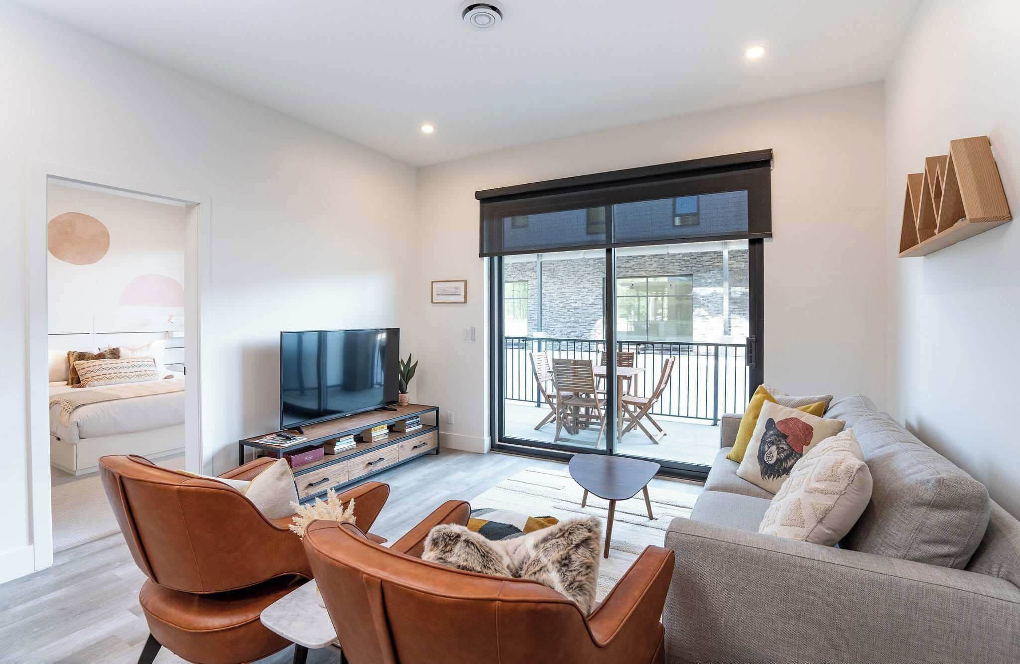 A modern living room with a TV, sofa, chairs, and a balcony with outdoor furniture.