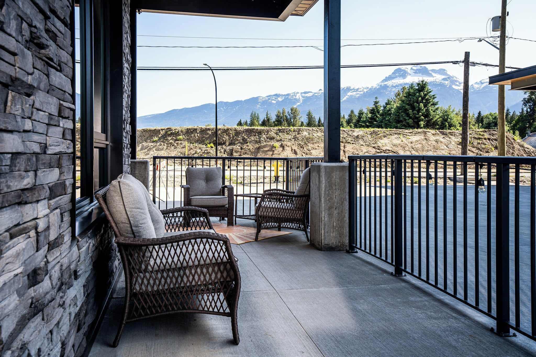 A balcony with wicker chairs, a view of a mountain range, and a stone wall.