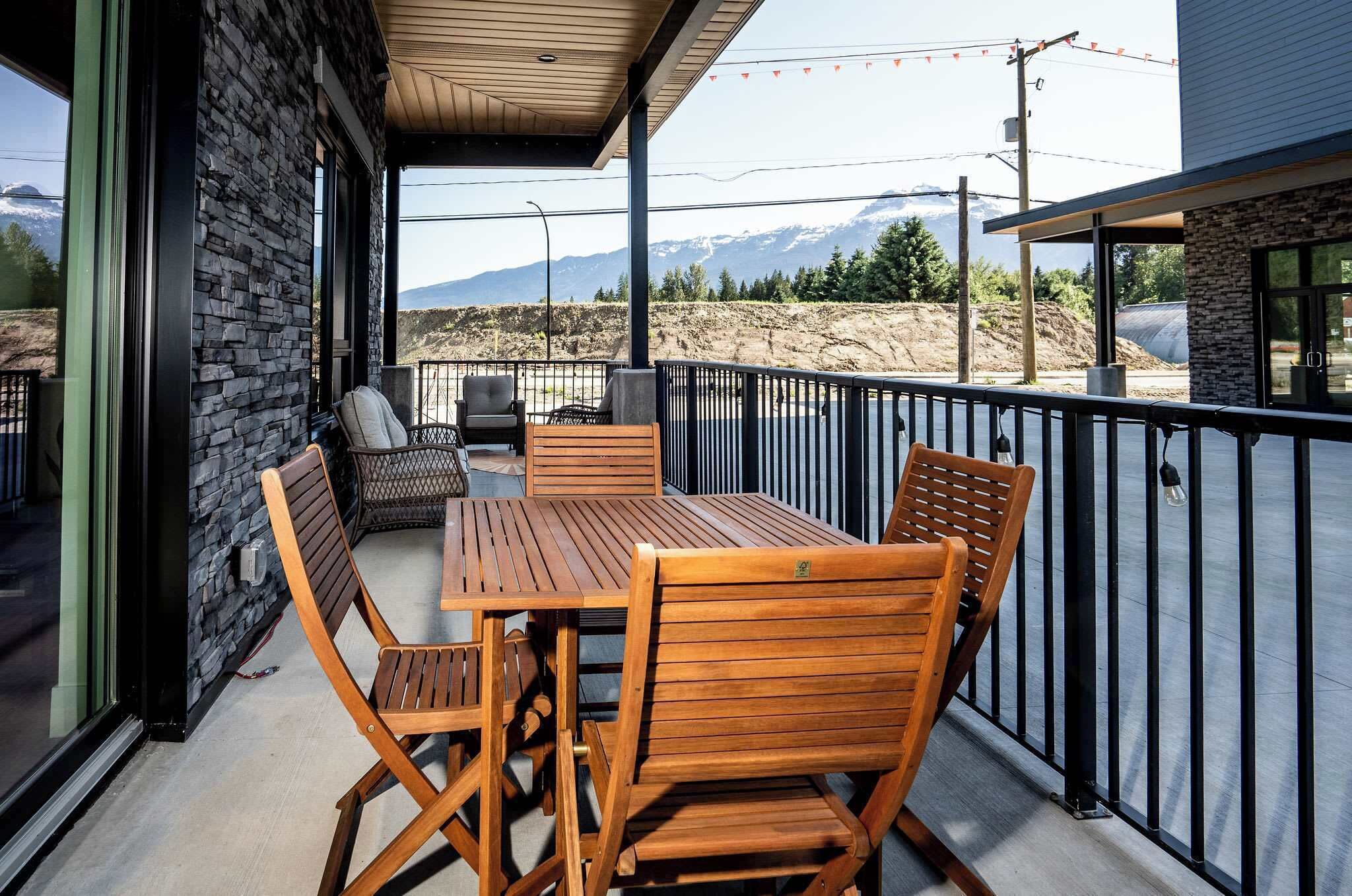 An outdoor patio with a wooden table and chairs, stone walls, and a view of mountains.