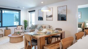 Ein modernes Wohnzimmer mit einem Holzesstisch, bequemen Sitzgelegenheiten und großen Fenstern.