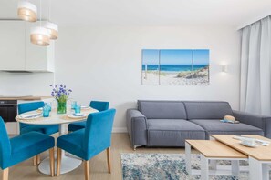 Un salon moderne avec un canapé gris, des fauteuils bleus, une table de salle à manger ronde et une décoration murale sur le thème de la plage.
