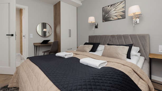 Un dormitorio moderno con una cama grande, lámparas de noche, un escritorio y un espejo.