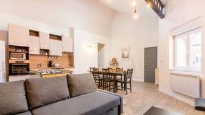 Une cuisine moderne dotée d’appareils électroménagers intégrés, un coin repas avec une table et des chaises, et un canapé gris dans un espace de vie lumineux.