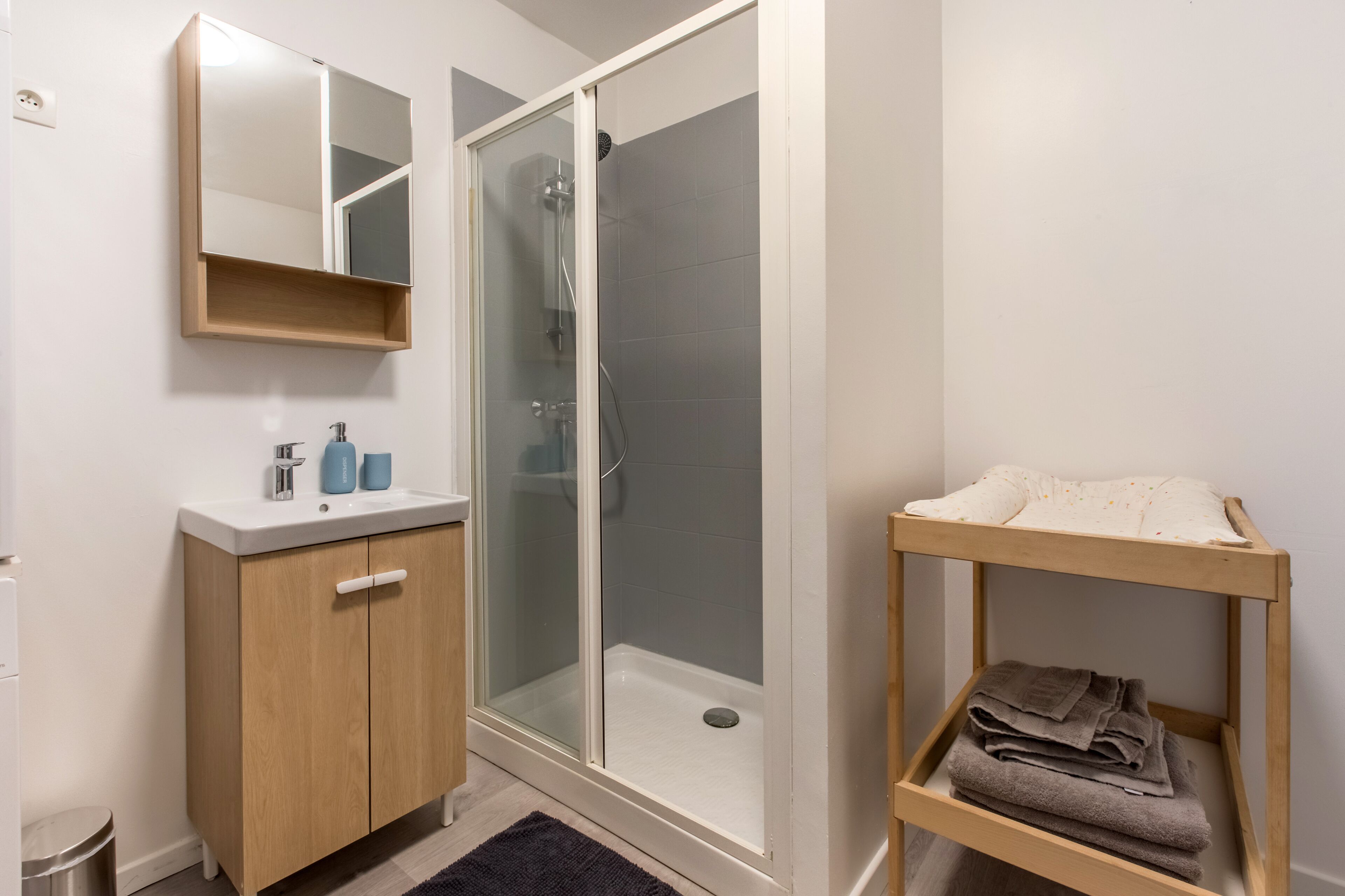 Een badkamer met een douche met glazen wand, een houten wastafelmeubel met spiegel en een plank met handdoeken.