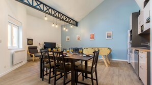 Un coin repas avec une table dressée pour quatre personnes, un canapé, un téléviseur et un espace cuisine équipé de placards et d’un lave-vaisselle.