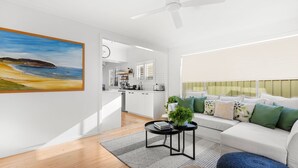 Un salon moderne avec un canapé, une table basse et un tableau représentant une scène de plage.