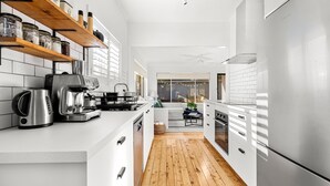 Une cuisine moderne avec des meubles blancs, un réfrigérateur en acier inoxydable, une machine à café et un plancher en bois.