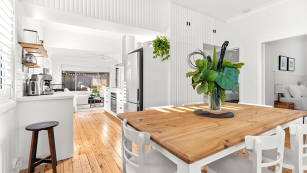 Une cuisine moderne avec des meubles blancs, une table à manger en bois et un îlot central agrémenté d’une plante.