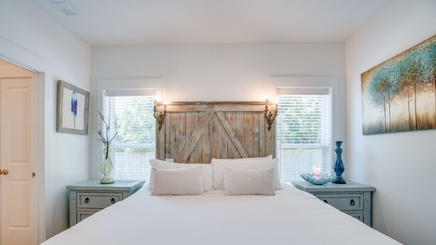 A bedroom with a large bed, two bedside tables, a wooden headboard, and a painting on the wall. - Seabreeze -Walk to beach! Pet friendly! (Panama City Beach)