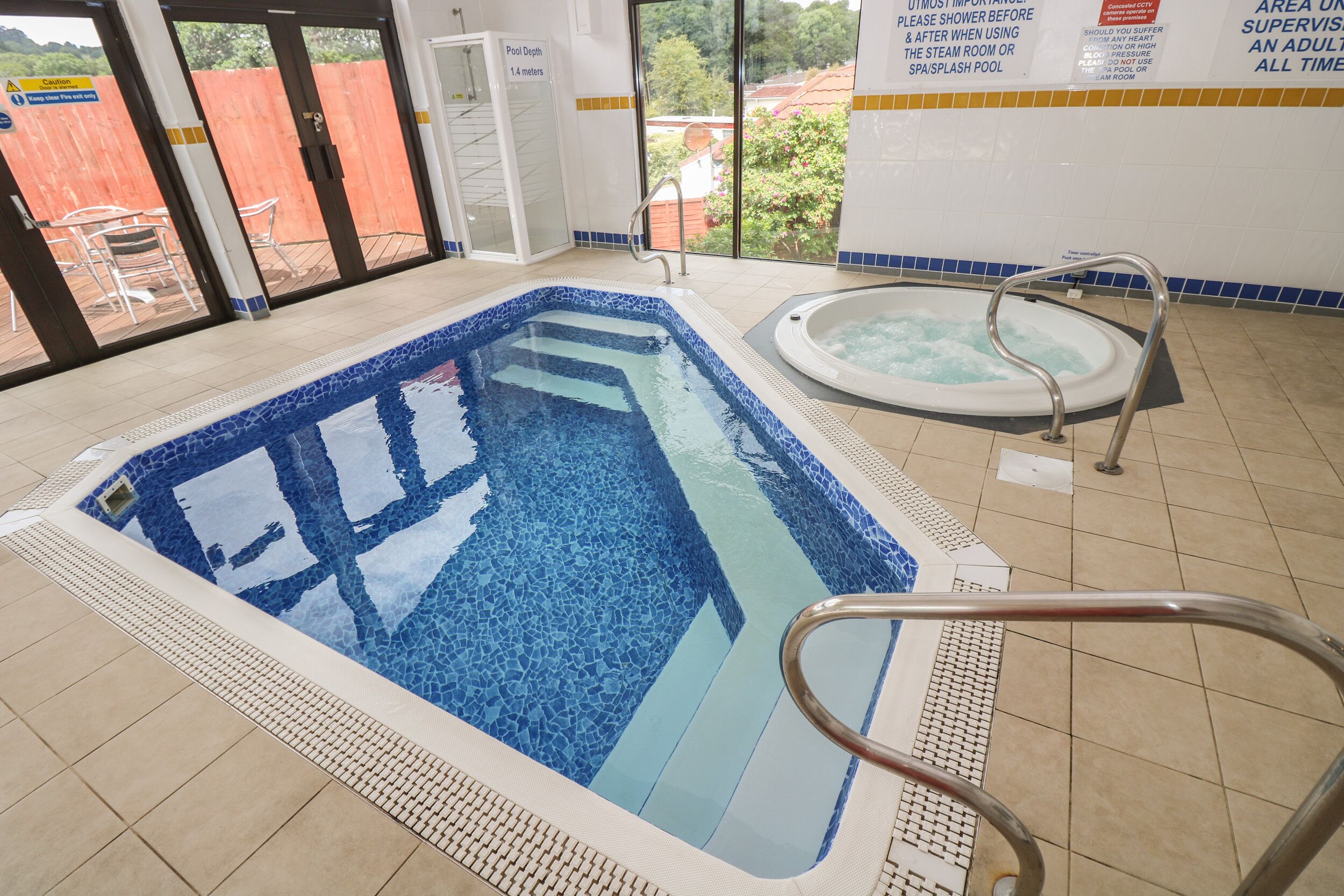 A swimming pool with a tiled edge, a hot tub, and a safety railing.
