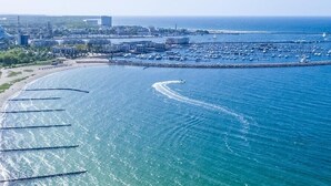 An aerial view of a coastal area with a marina, a large cruise ship docked, and a curved breakwater extending into the sea. - Hotel Am Kai 334 (Rostock)