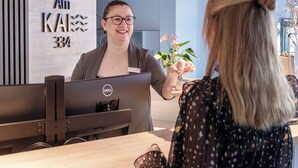 A reception desk with a Dell computer, a sign reading "Am KAI 334", and a potted plant. - Hotel Am Kai 334 (Rostock)