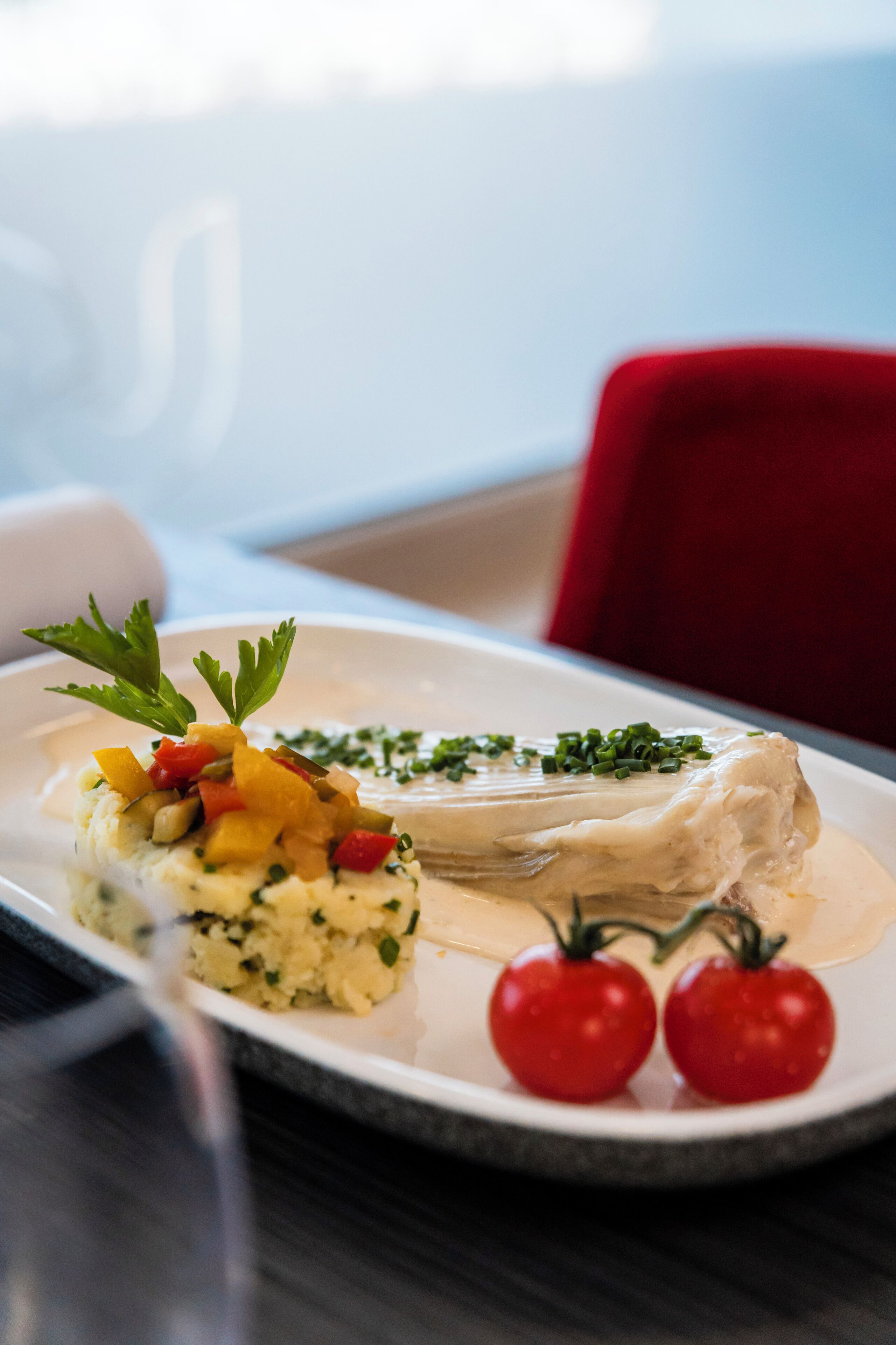 A white plate with a fish fillet, mashed potatoes, and cherry tomatoes on a table.
