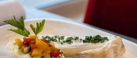 A white plate with a fish fillet, mashed potatoes, and cherry tomatoes on a table.