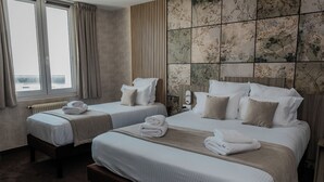 A hotel room with two beds, a large window, and a tiled wall.