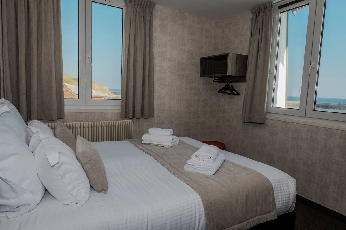 Ein Hotelzimmer mit einem großen Bett, zwei Vorhängen und einem Meerblick. Ein Fernseher ist an der Wand montiert.