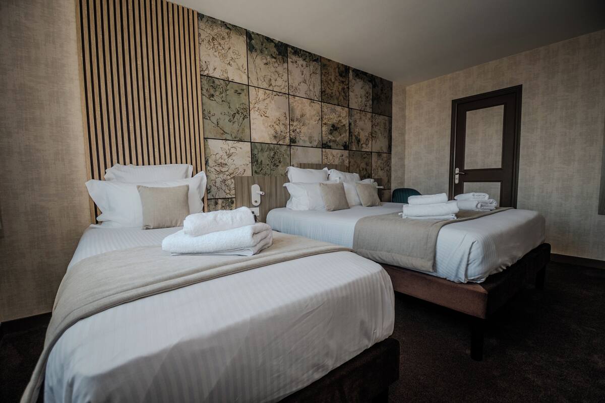Ein Hotelzimmer mit drei Betten, jeweils mit weißer Bettwäsche und Kissen, einem Holz-Kopfteil und einer großen Wanddekoration.