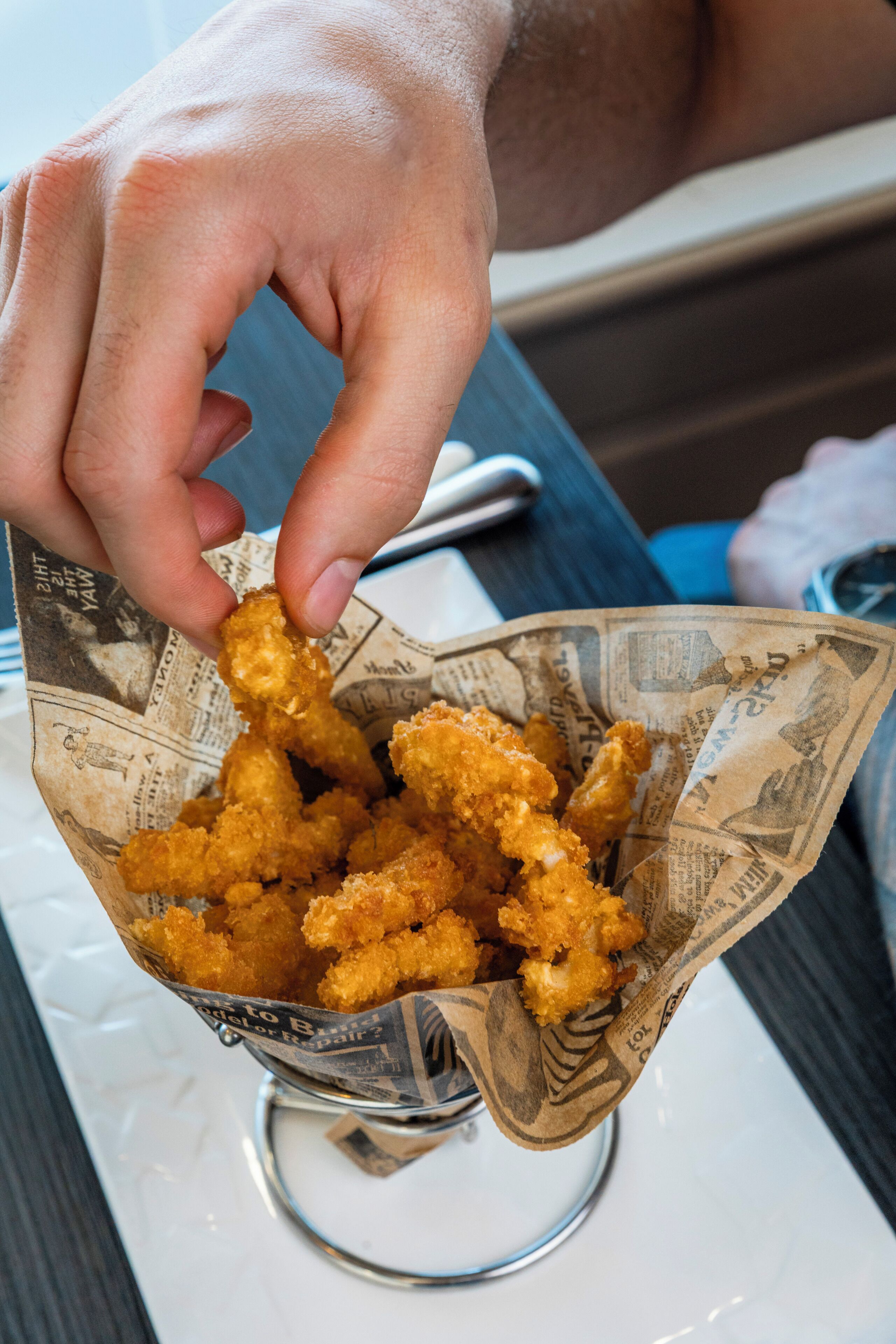 A hand holding a basket of fried chicken pieces.