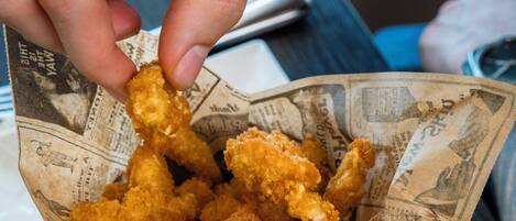 A hand holding a basket of fried chicken pieces.