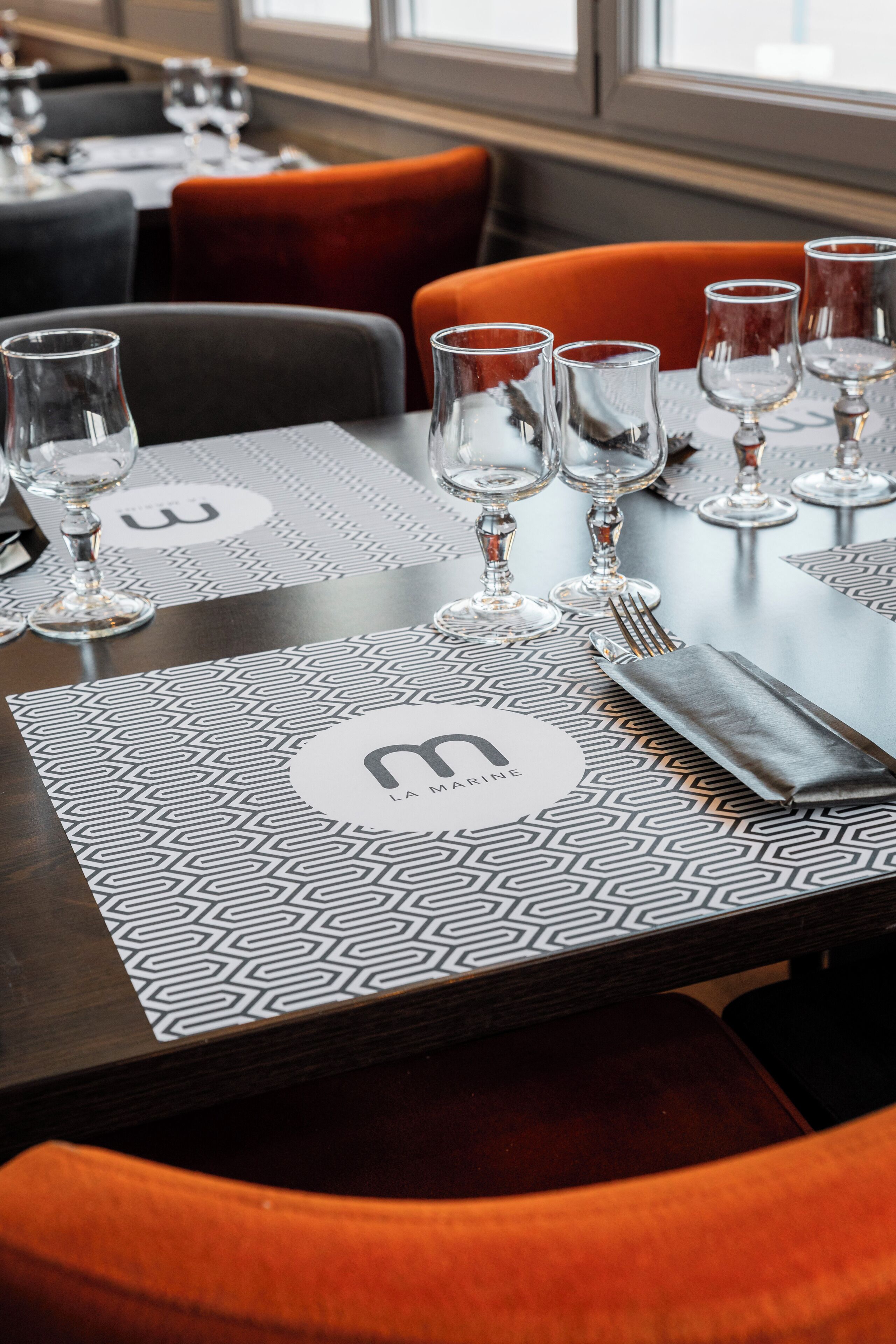 A restaurant table set with wine glasses, cutlery, and a placemat with a logo.