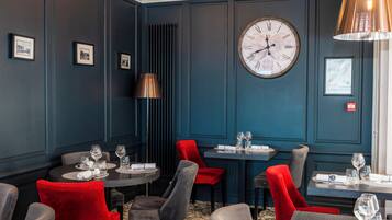 Un espace repas avec des murs bleu foncé, une grande horloge murale et des chaises rouges et grises.