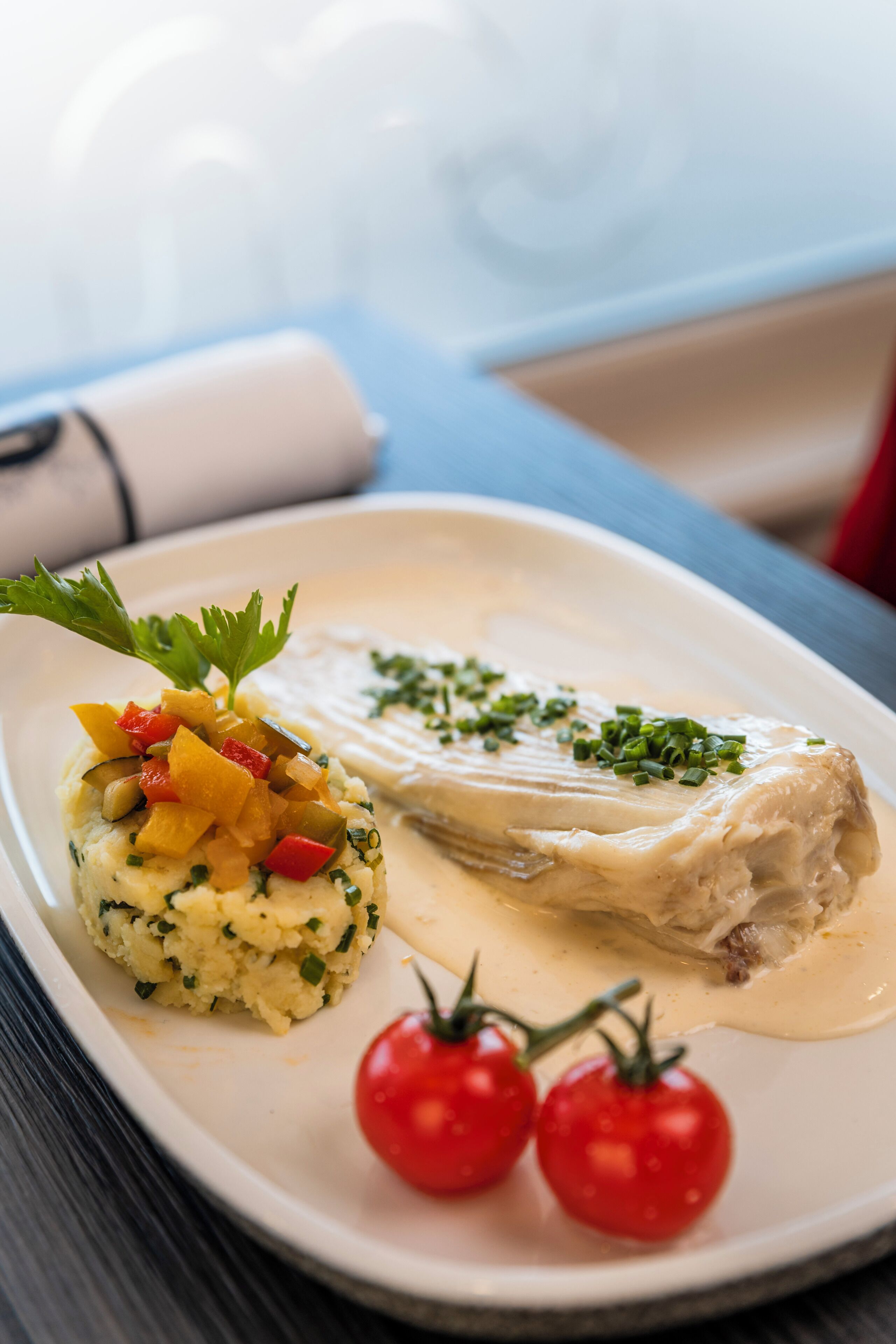 A plate with fish, mashed potatoes, and cherry tomatoes.