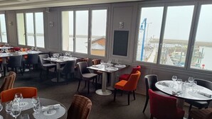 A restaurant with multiple tables and chairs, large windows with a view of the harbor, and a modern interior design.