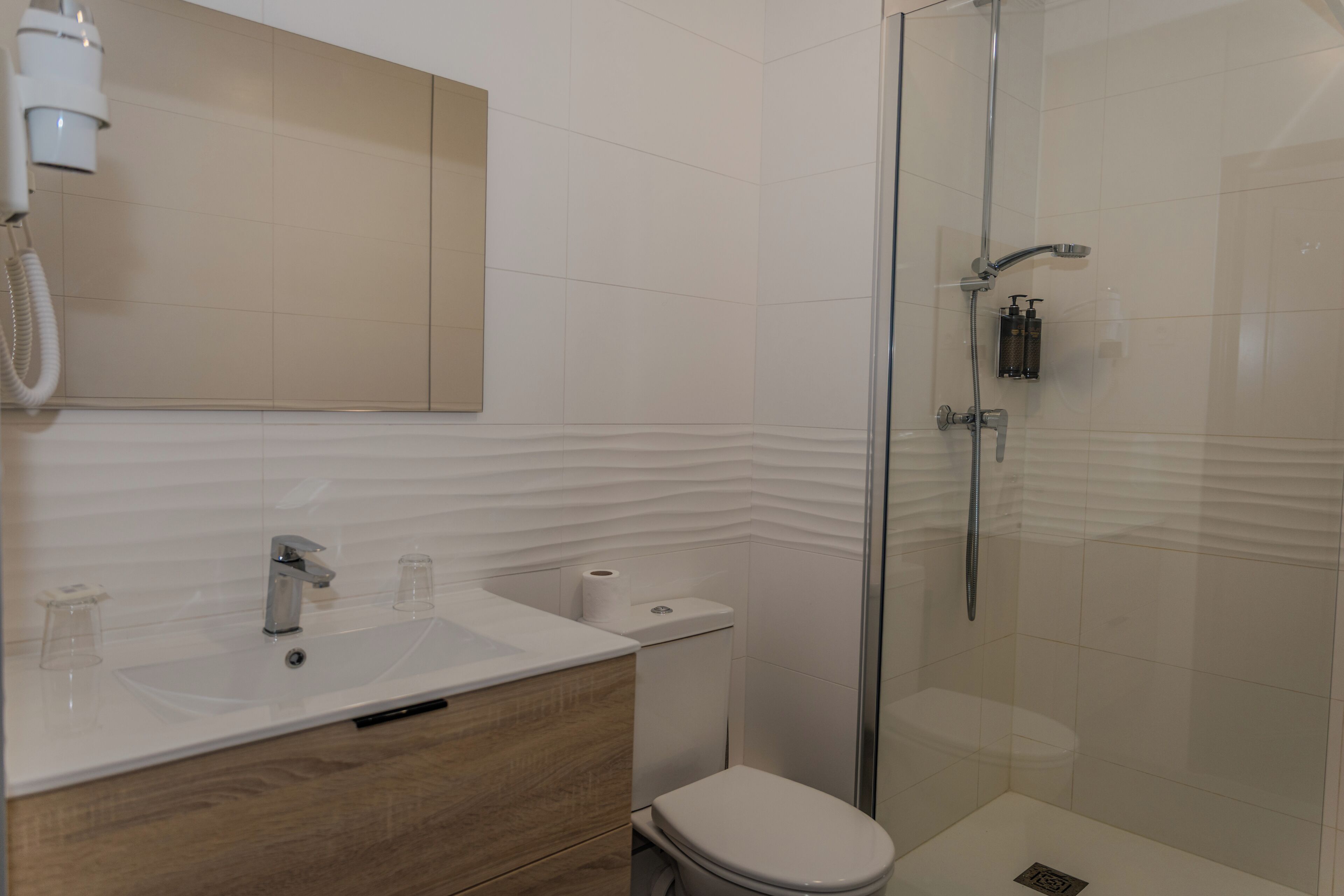A modern bathroom with a glass-enclosed shower, a white sink with a mirror above it, and a toilet with a beige wall.