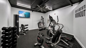 Un gimnasio con equipo de ejercicio, televisión y un letrero motivacional en la pared.