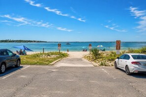 Ein Zugang zum Strand mit Parkplatz, blauem Himmel und ruhiger See.