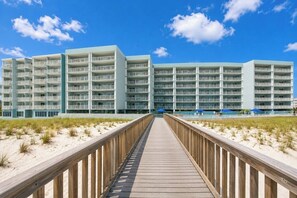 A beachfront hotel with multiple balconies, a wooden boardwalk leading to the entrance, and a clear blue sky. - Okaloosa Island Gulf Front Paradise Studio Condo (Fort Walton Beach)