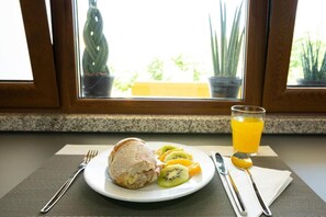 Un desayuno con un plato de comida, un vaso de zumo de naranja y vistas a plantas en macetas desde la ventana.