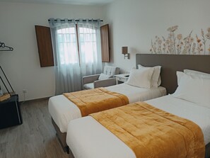 Habitación de hotel con dos camas, un escritorio, una silla, una lámpara y un ventanal con cortinas.