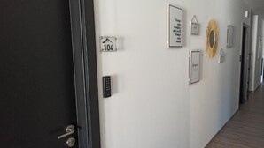 A hallway with a black door, a keypad, and several framed items on the wall, including a sign with the number 104. - Porto d'Abrigo - Alojamento Local (Sardoal)