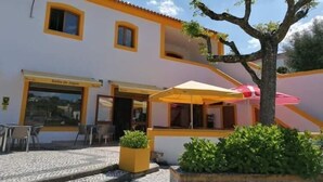 A building with a yellow and white facade, a tiled patio area, outdoor seating, and a tree. - Porto d'Abrigo - Alojamento Local (Sardoal)