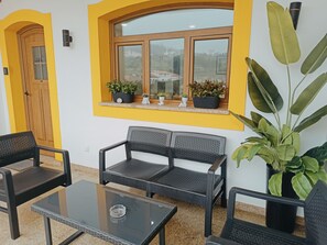 Una habitación con una paleta de colores amarillo y blanco, que incluye un ventanal con plantas en macetas, un sofá y una mesa.