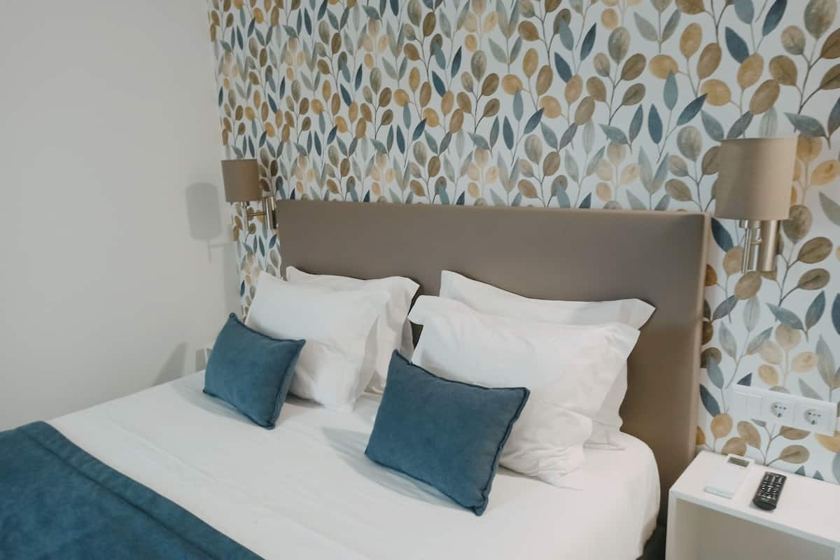 A neatly made bed with white and blue pillows, a brown headboard, and a white bedside table with a remote control.
