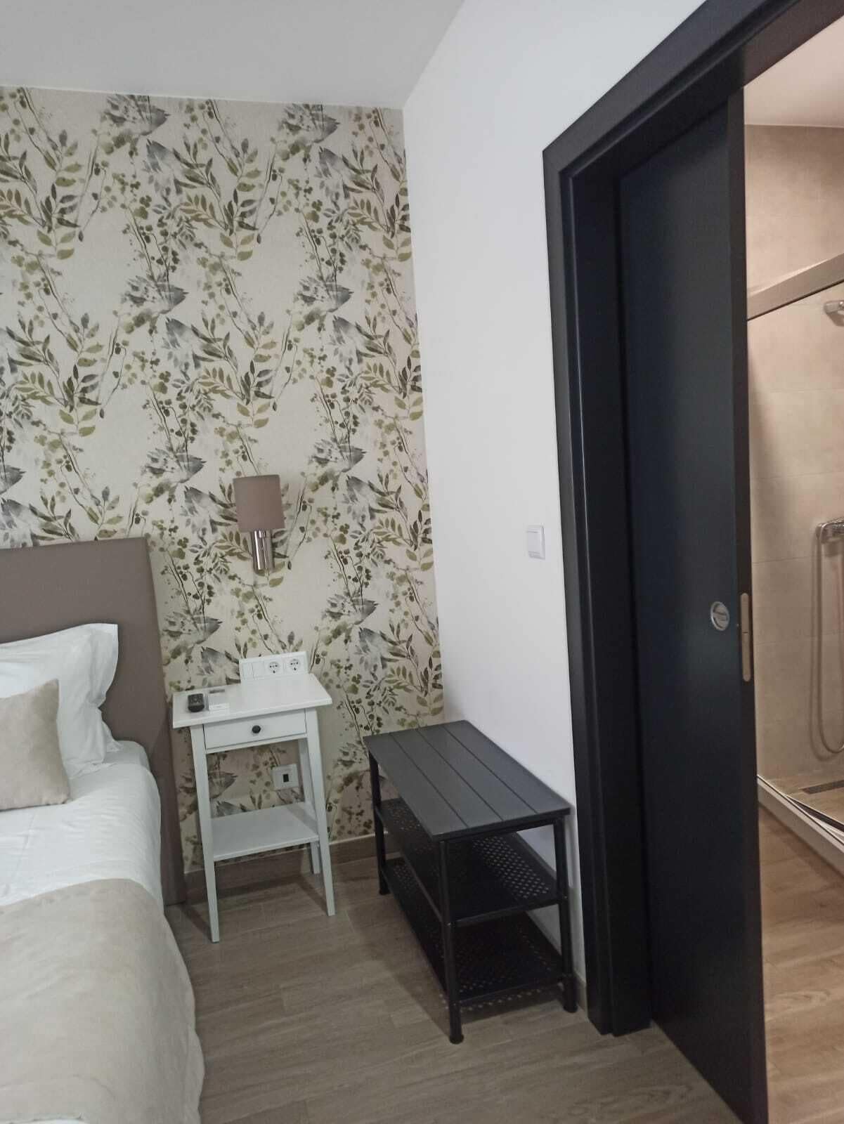 Une chambre d’hôtel avec un lit, un petit bureau blanc avec une lampe, une table noire et un espace douche.