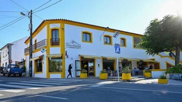 Un edificio con una cafetería llamada "Puro D'Albuquerque" en la planta baja, con fachada amarilla y blanca, mesas al aire libre y un paso de peatones.