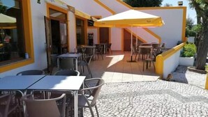 An outdoor patio area with tables and chairs, a yellow umbrella, and a building entrance labeled "Salão de João." - Porto d'Abrigo - Alojamento Local (Sardoal)