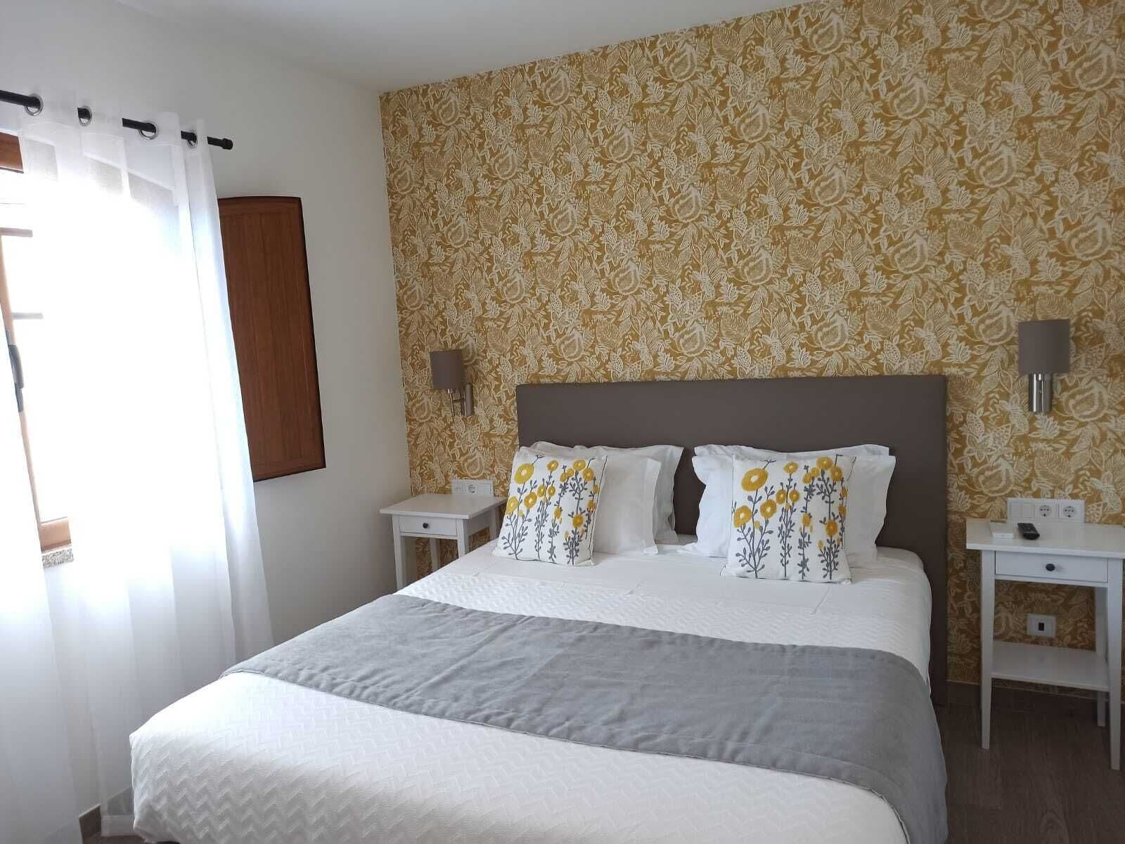 Une chambre à coucher bien rangée, avec un grand lit, deux tables de chevet et une lampe fixée au mur.