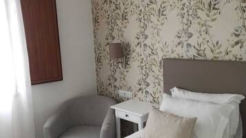 Una habitación de hotel con una cama, una silla, una mesita y un papel tapiz floral en la pared.