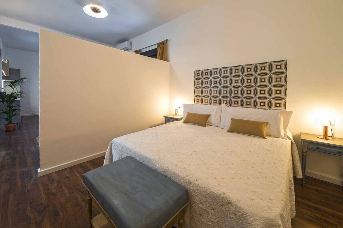 Un dormitorio con cama, mesitas de noche, un banco y un panel decorativo en la pared.
