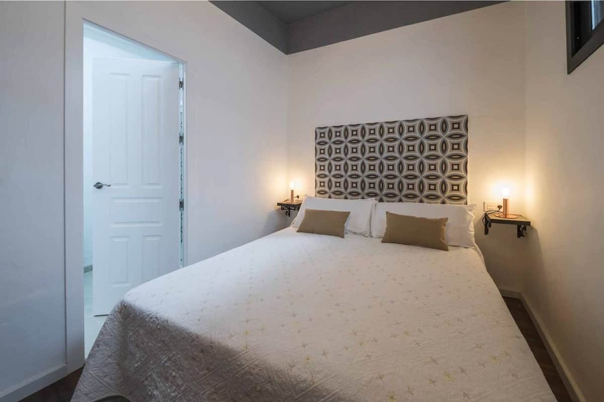 Un dormitorio con una cama, dos mesitas de noche, un cabecero estampado y una puerta.