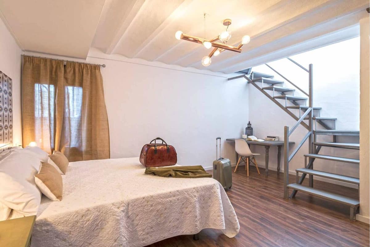Un dormitorio con cama, escritorio, maleta y una escalera.