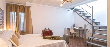 A bedroom with a bed, a desk, a suitcase, and a staircase.