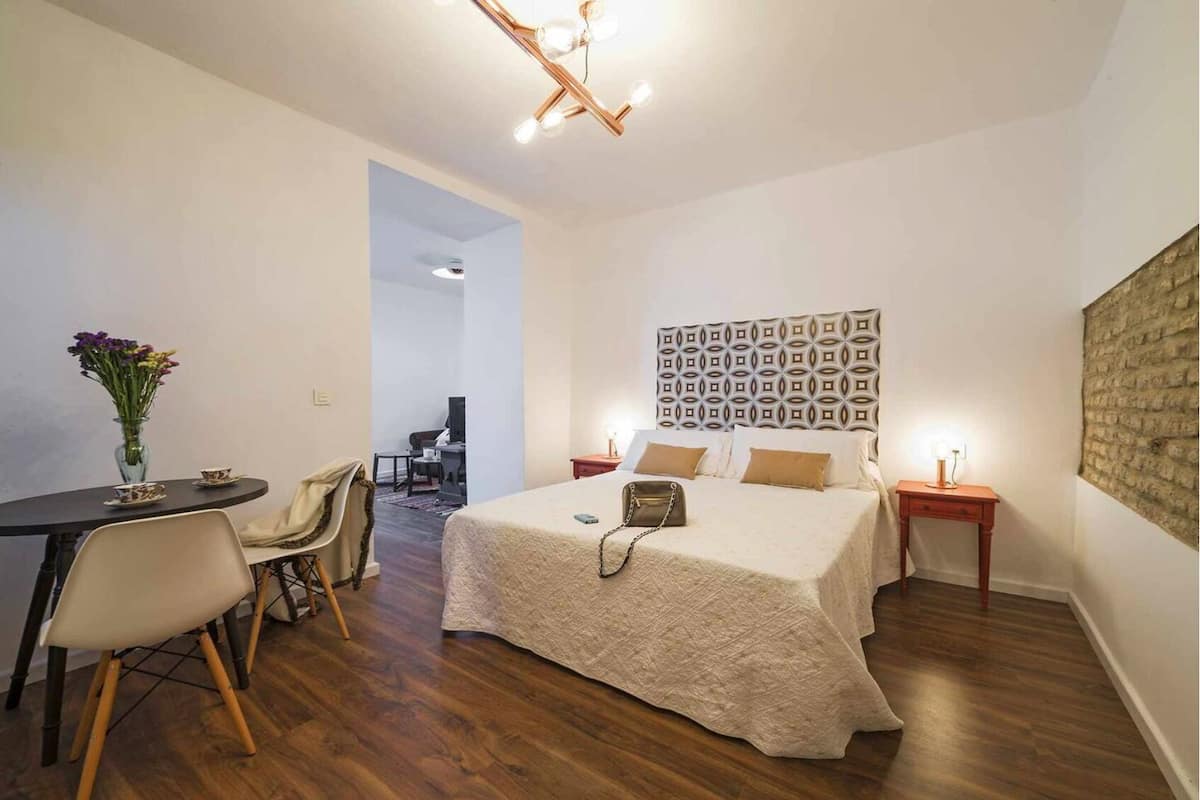Habitación de hotel con cama, mesitas de noche, escritorio con silla, un florero y una pared de ladrillo.