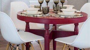 Una mesa de comedor con mantel rojo, rodeada de sillas blancas de patas de madera.