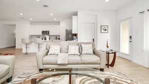 A modern living room with a beige sofa, a glass coffee table, and a patterned rug.