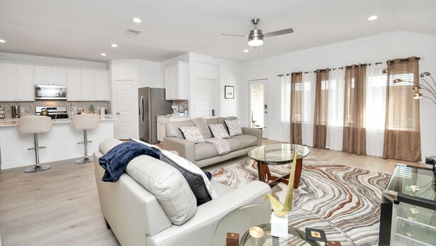 A modern living room with a sofa, a glass coffee table, and a dining area with a chandelier.
